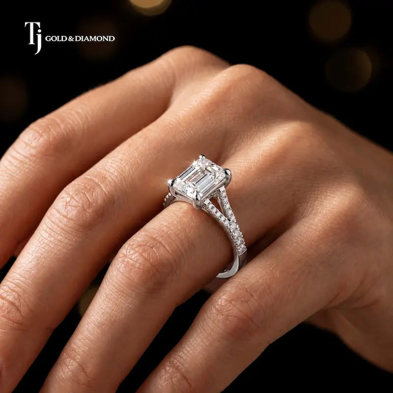 Emerald cut split shank lab-grown diamond engagement ring worn on hand in 18kt white gold.