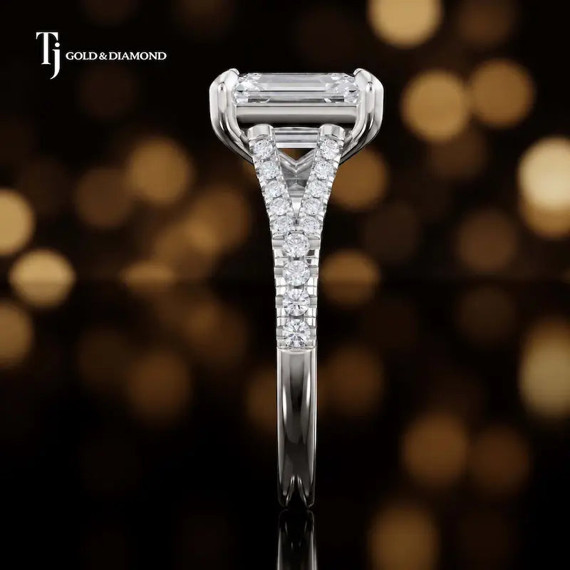 Side profile of an emerald cut split shank lab-grown diamond engagement ring with diamond-set shoulders in 18kt white gold.