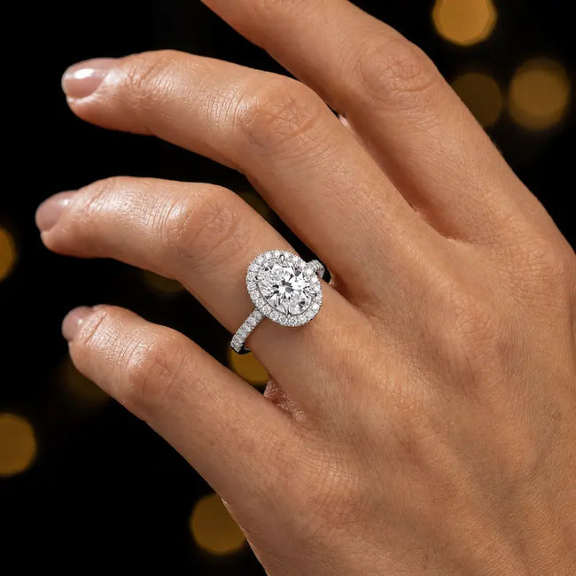 Oval cut halo lab-grown diamond engagement ring worn on hand in 18kt white gold.