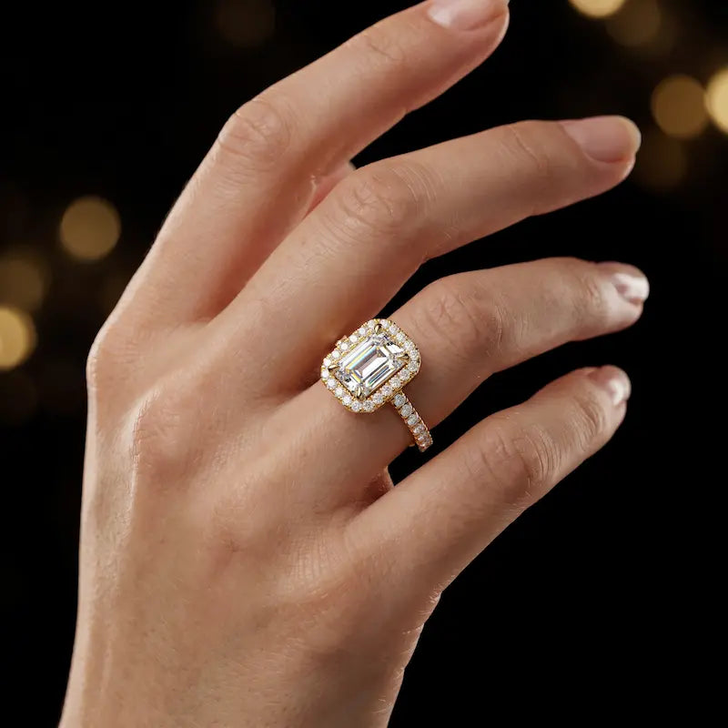 Emerald cut halo lab-grown diamond engagement ring worn on hand in 18kt yellow gold.
