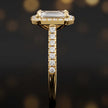 Side profile of an emerald cut halo lab-grown diamond engagement ring with diamond-set shoulders in 18kt yellow gold.