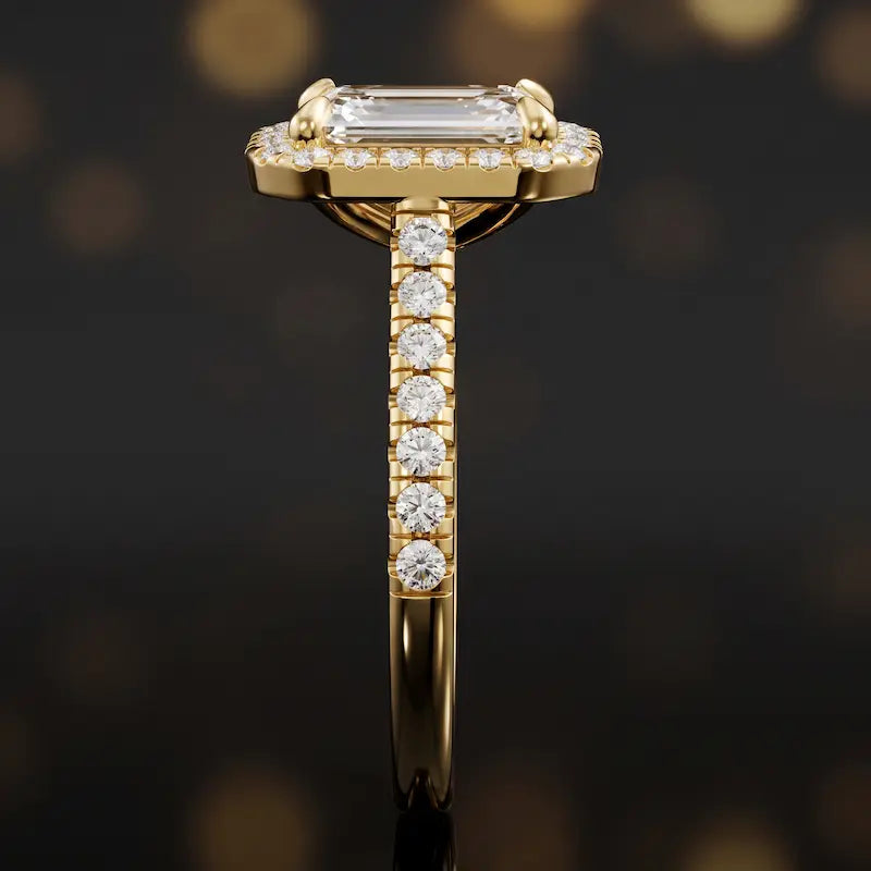 Side profile of an emerald cut halo lab-grown diamond engagement ring with diamond-set shoulders in 18kt yellow gold.