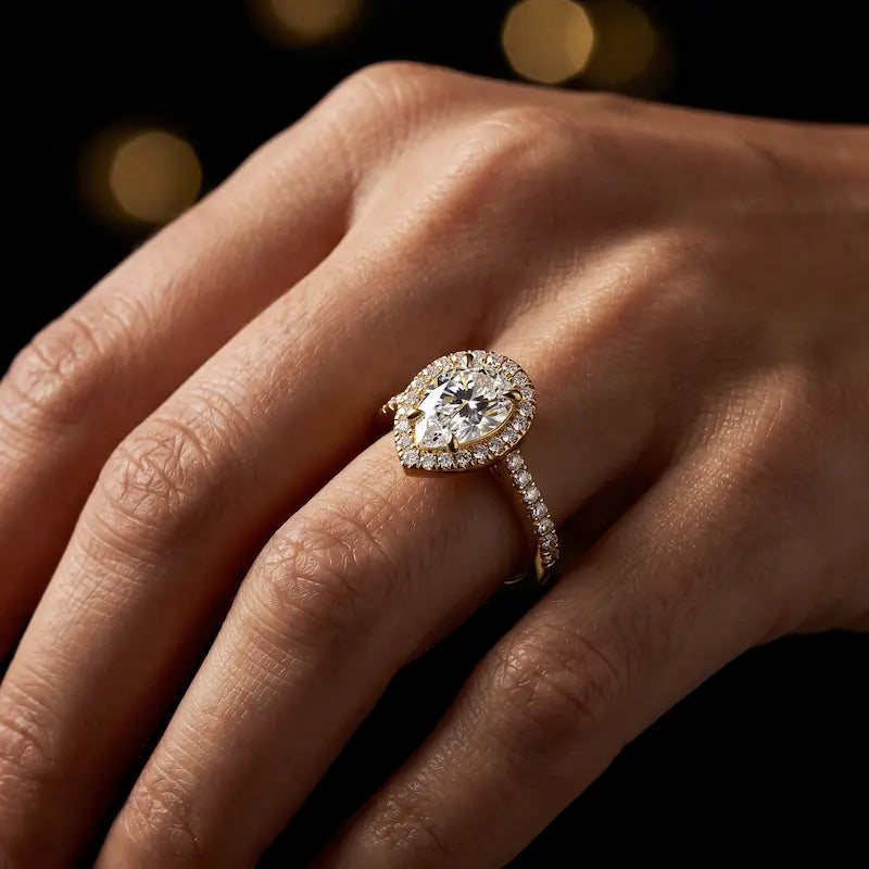 Pear cut halo lab-grown diamond engagement ring worn on hand in 18kt yellow gold.