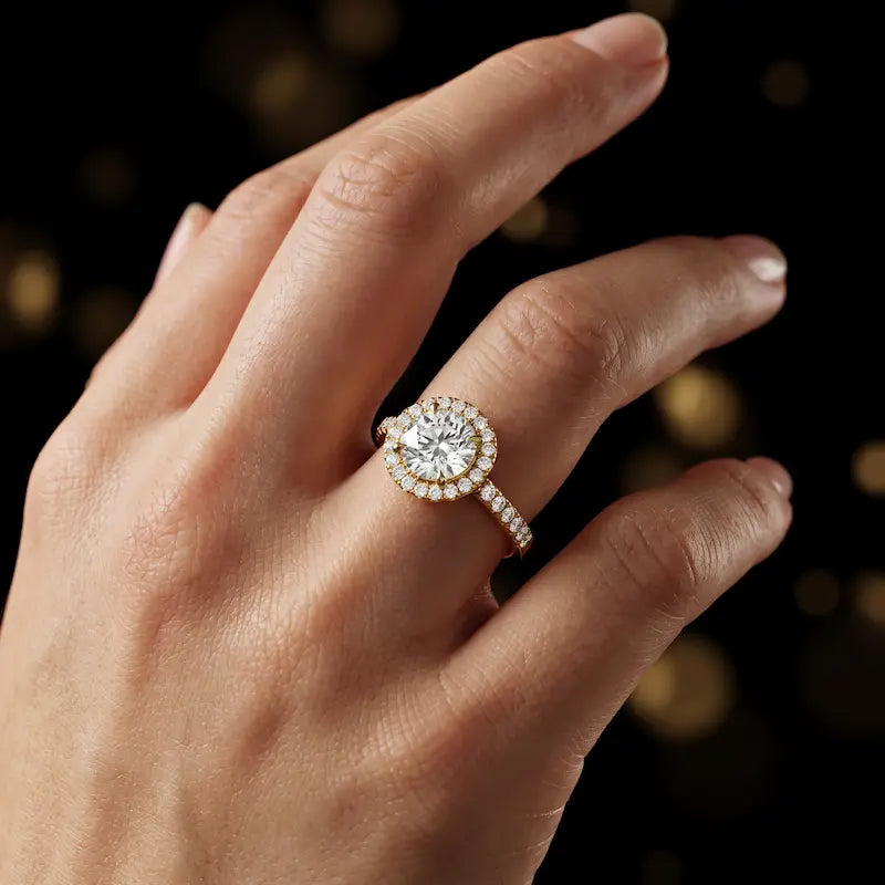 Round cut halo lab-grown diamond engagement ring worn on hand in 18kt yellow gold.