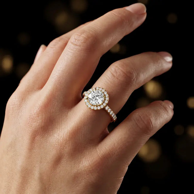 Round cut halo lab-grown diamond engagement ring worn on hand in 18kt yellow gold.
