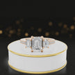 360-degree rotating view of an emerald cut three-stone lab-grown diamond engagement ring in 18kt rose gold with diamond shoulders